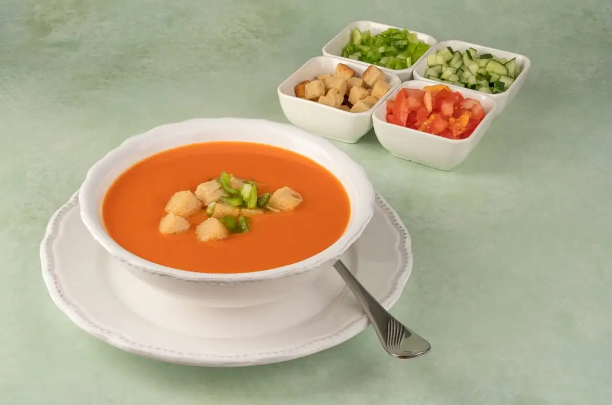 Andalusian gazpacho, served on a white plate and displayed with its healthy ingredients