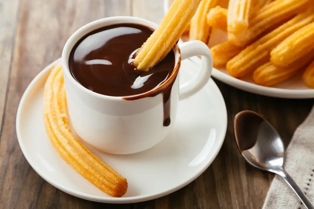 Churros espanhóis tradicionais com calda de chocolate quente em uma mesa rústica de madeira